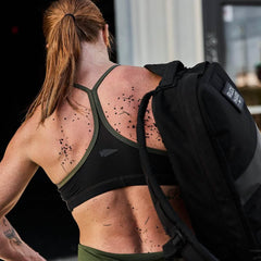 Woman with brown hair wearing a GORUCK rucksack, in athletic gear with grass on her back.