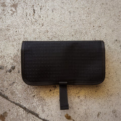 A closed Scars Wire Dopp, an EDC pouch with a strap made from black waxed twill, rests on a textured concrete surface.