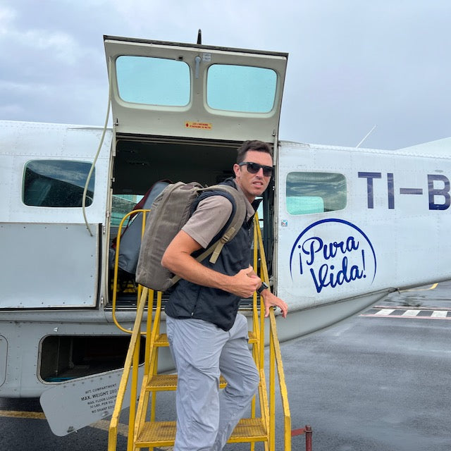 Man with sunglasses and a GR1 USA - Heritage Waxed Canvas backpack boards a small airplane with 