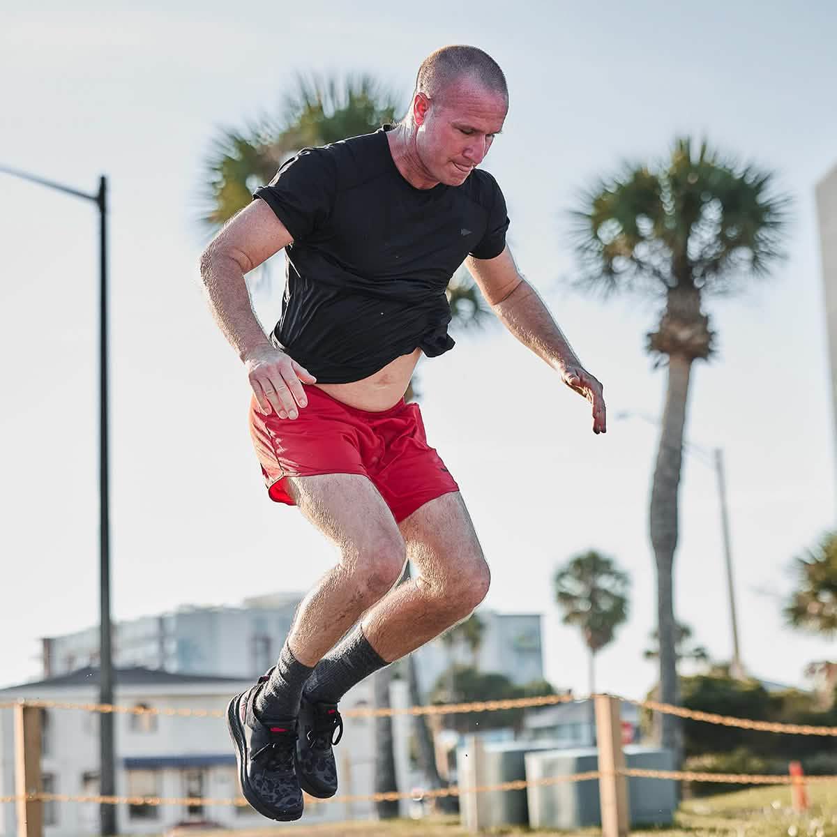 Man doing outdoor fitness workout in GORUCK gear, black shirt and red shorts, palm trees background