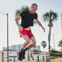 Man doing outdoor fitness workout in GORUCK gear, black shirt and red shorts, palm trees background