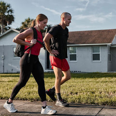Man and woman rucking outdoors with GORUCK backpacks, walking on sidewalk in athletic wear