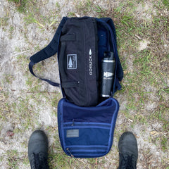 On grass, an open backpack reveals Simple Training Sandbags and a water bottle inside—ideal for sandbag workouts or your home gym. Black boots are visible below.