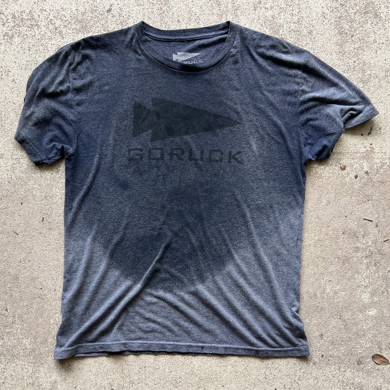 A dark gray Three Rules Tee - Unisex Tri-BlendX with wet spots, laid flat on concrete—a cool essential for those who never get lost.