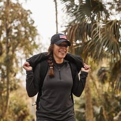 Woman rucking outdoors with GORUCK gear, wearing black cap and backpack on forest trail