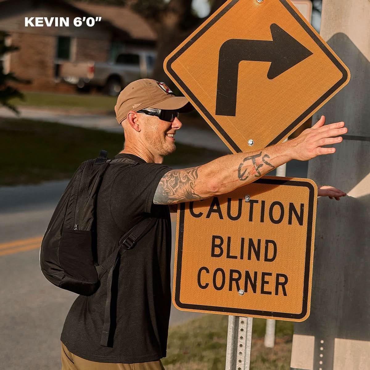 Man in GORUCK gear with backpack stands by caution blind corner sign outdoors