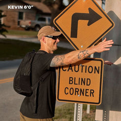 Man in GORUCK gear with backpack stands by caution blind corner sign outdoors