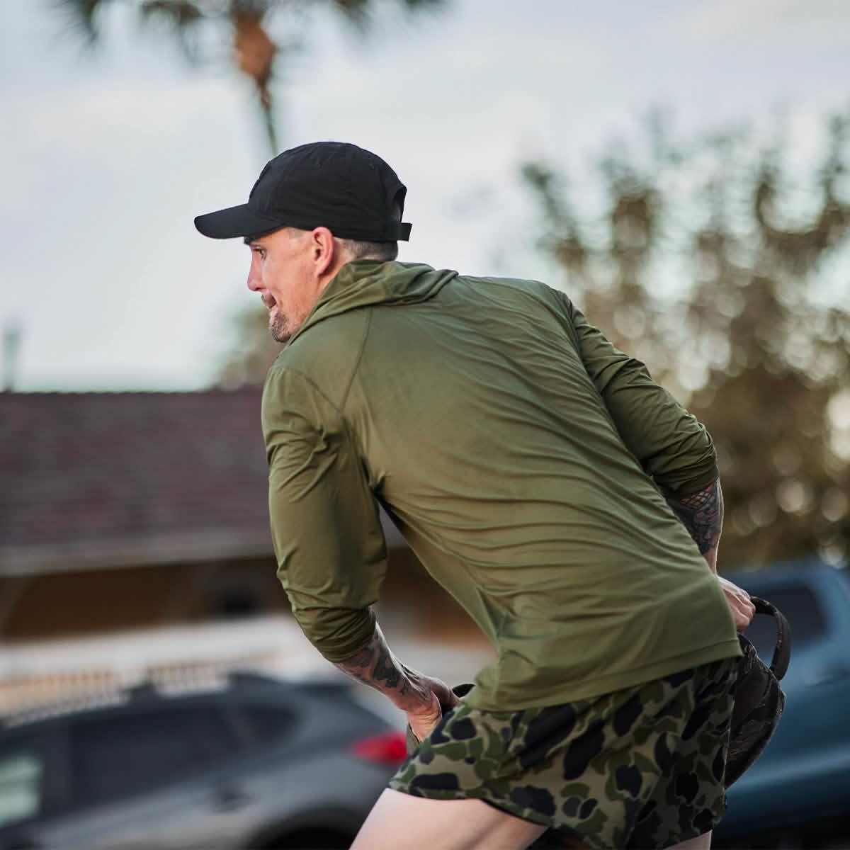 Man outdoors in GORUCK ToughMesh Hoodie, olive green, camo shorts, black cap