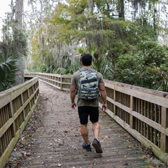 Man rucking in forest with GORUCK camo backpack on wooden trail bridge