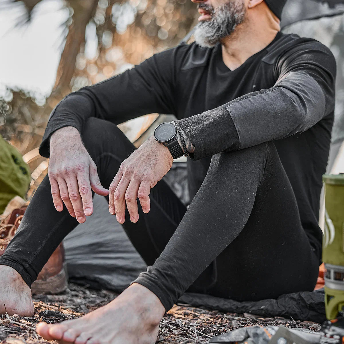 Man outdoors in black Merino wool base layer leggings by GORUCK, seated near camping gear.