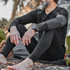 Man outdoors in black Merino wool base layer leggings by GORUCK, seated near camping gear.