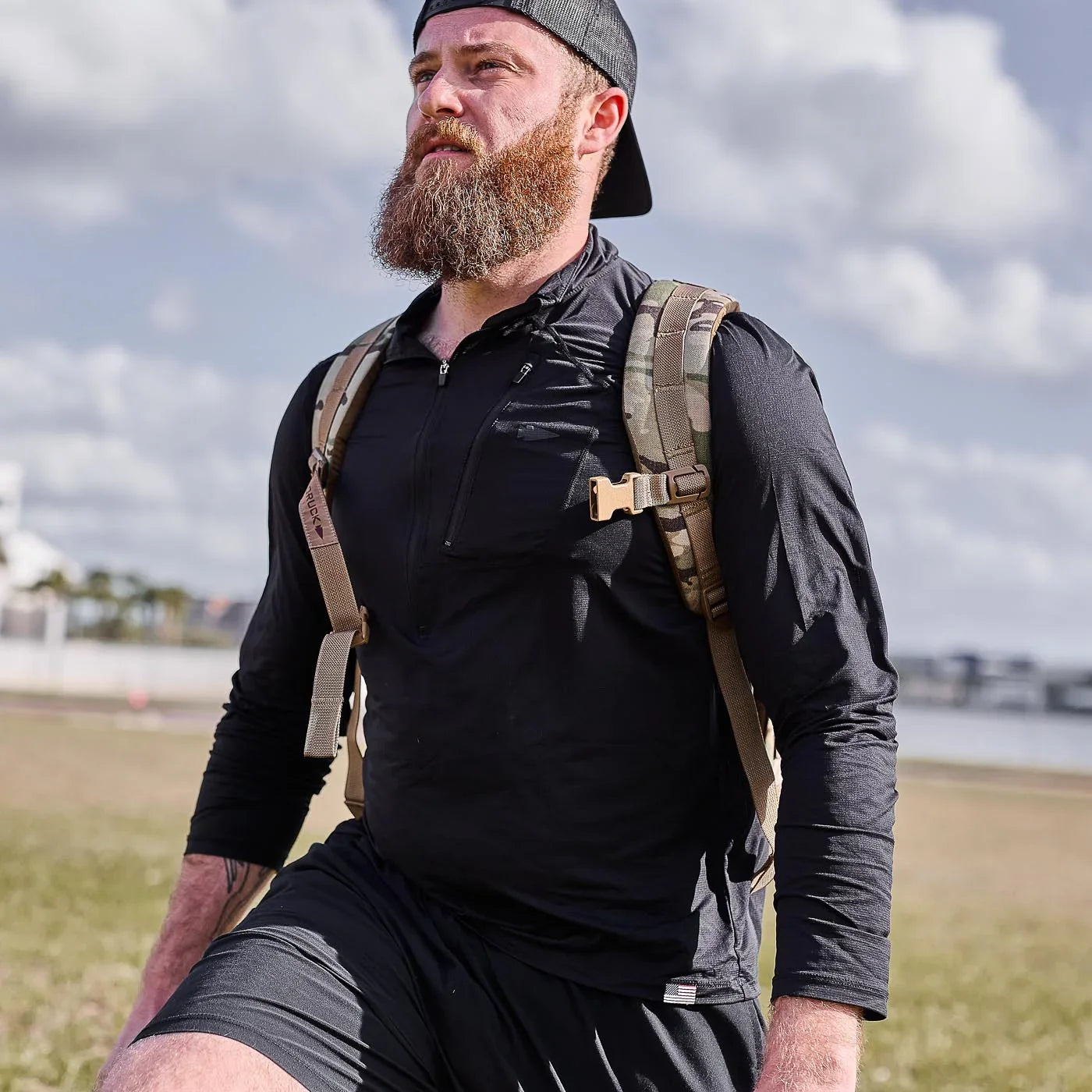 Man outdoors wearing GORUCK men's USA long sleeve performance half zip with rucksack