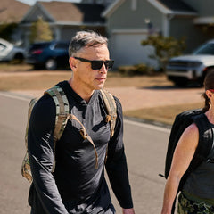 Man wearing GORUCK sun hoodie and rucksack walking outdoors in suburban neighborhood