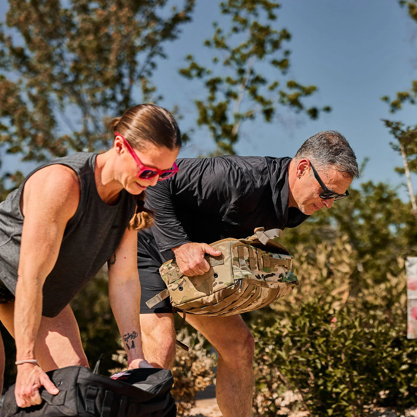 Two people outdoors in GORUCK activewear lifting rucksacks during fitness training