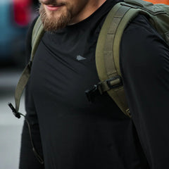 Man wearing GORUCK men's black long sleeve performance tee and olive rucksack outdoors