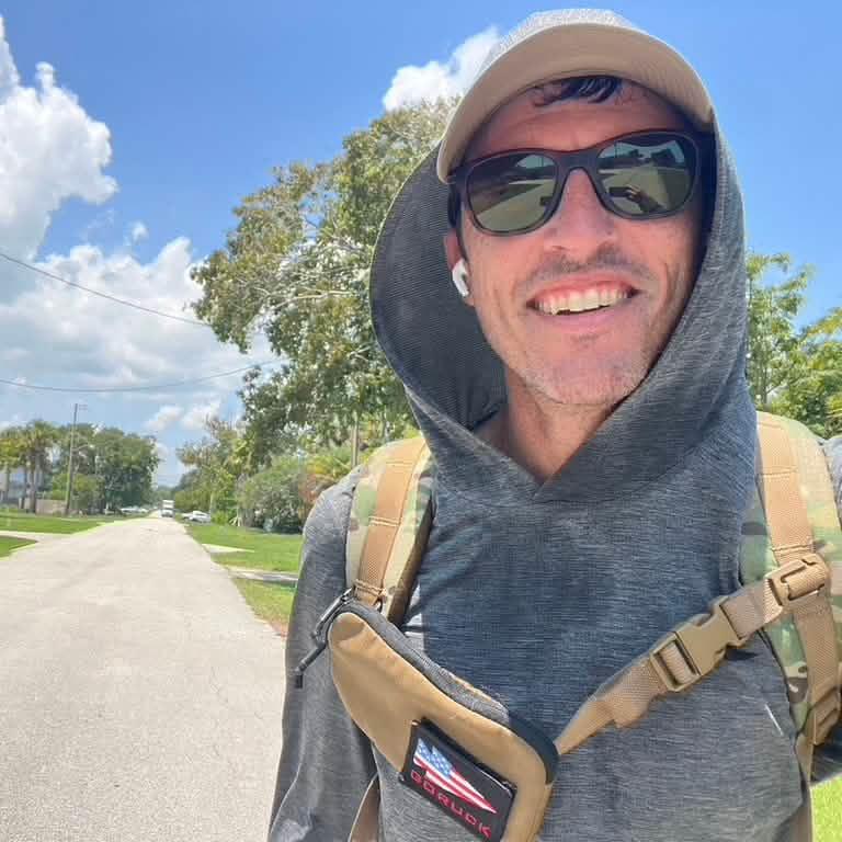 Man outdoors in GORUCK sun hoodie, sunglasses, and rucking backpack on a sunny street