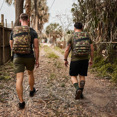 Two men rucking outdoors with GORUCK camo backpacks on a dirt trail, wearing activewear.