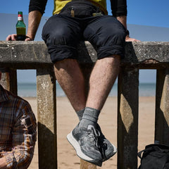 Man wearing GORUCK charcoal Merino wool socks and sneakers sitting on a beach wall