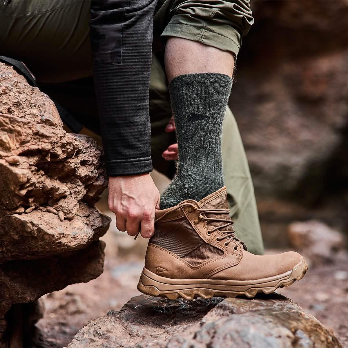 Man wearing green Merino wool GORUCK socks and brown boots outdoors on rocky terrain