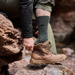 Man wearing green Merino wool GORUCK socks and brown boots outdoors on rocky terrain