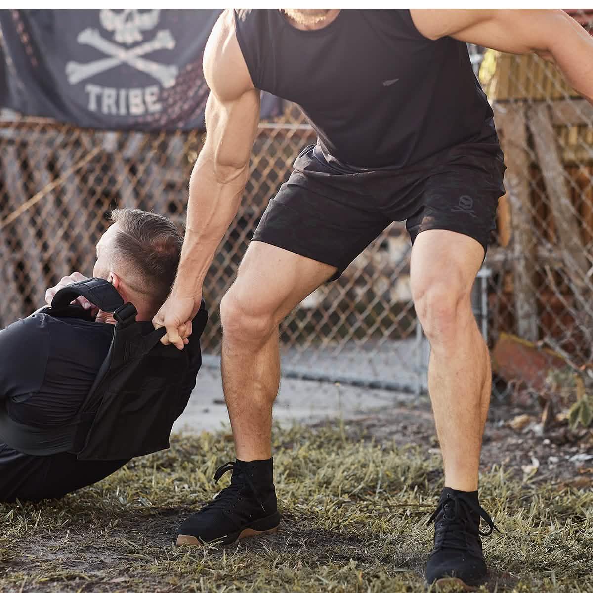 GORUCK athletes in outdoor rucking training, one assisting another, with tactical gear.