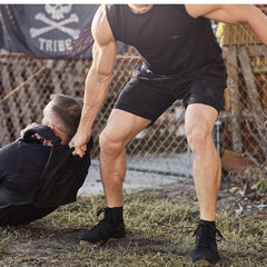 GORUCK athletes in outdoor rucking training, one assisting another, with tactical gear.