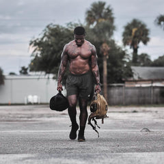 Athletic man rucking outdoors with GORUCK sandbag and backpack, palm trees in background.