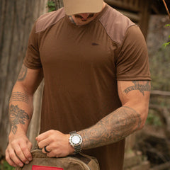 Man in a brown GORUCK rucking shirt outdoors, wearing a watch, carrying a rucksack