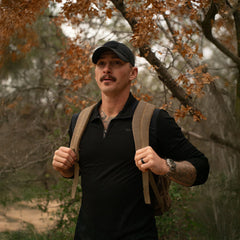 Man rucking outdoors with GORUCK backpack, wearing black cap and shirt in autumn woods