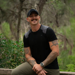 Man in GORUCK athletic gear with tattoos, smiling outdoors in a forest setting