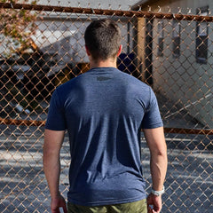 Man in navy GORUCK t-shirt standing outdoors by a rusted chain-link fence