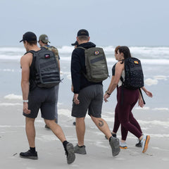 Group wearing GORUCK backpacks rucking on sandy beach by ocean