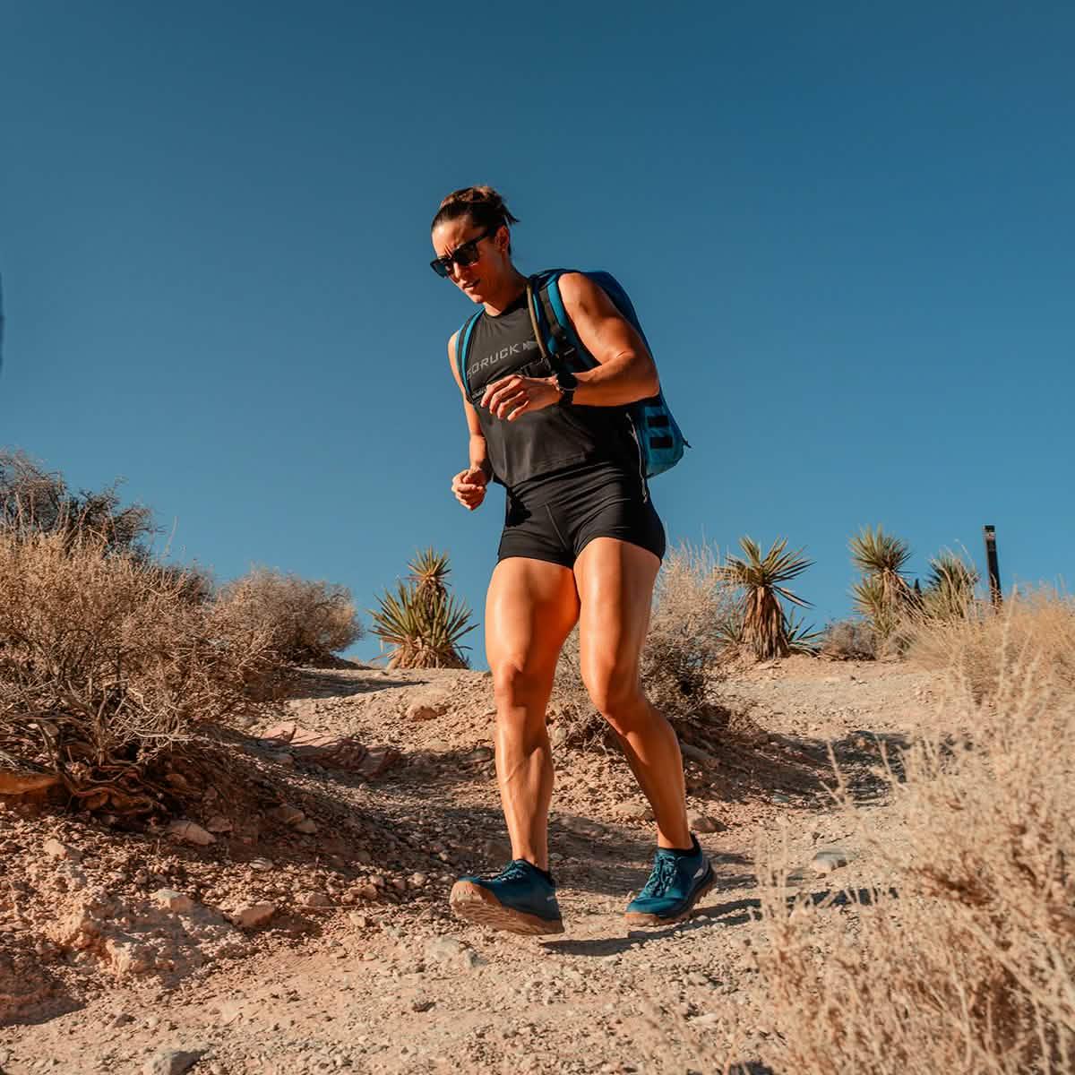 Woman rucking outdoors in GORUCK gear on a desert trail under clear blue sky