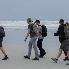 GORUCK team rucking with backpacks along a sandy beach on a cloudy day