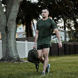 Man wearing olive GORUCK Tough Mesh Tee, carrying rucksack outdoors on grass