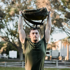 Man outdoors lifting rucksack overhead wearing olive GORUCK Tough Mesh Tee