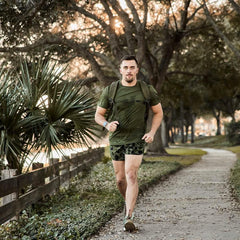 Man rucking in GORUCK olive Tough Mesh Tee outdoors, wearing rucksack on tree-lined path