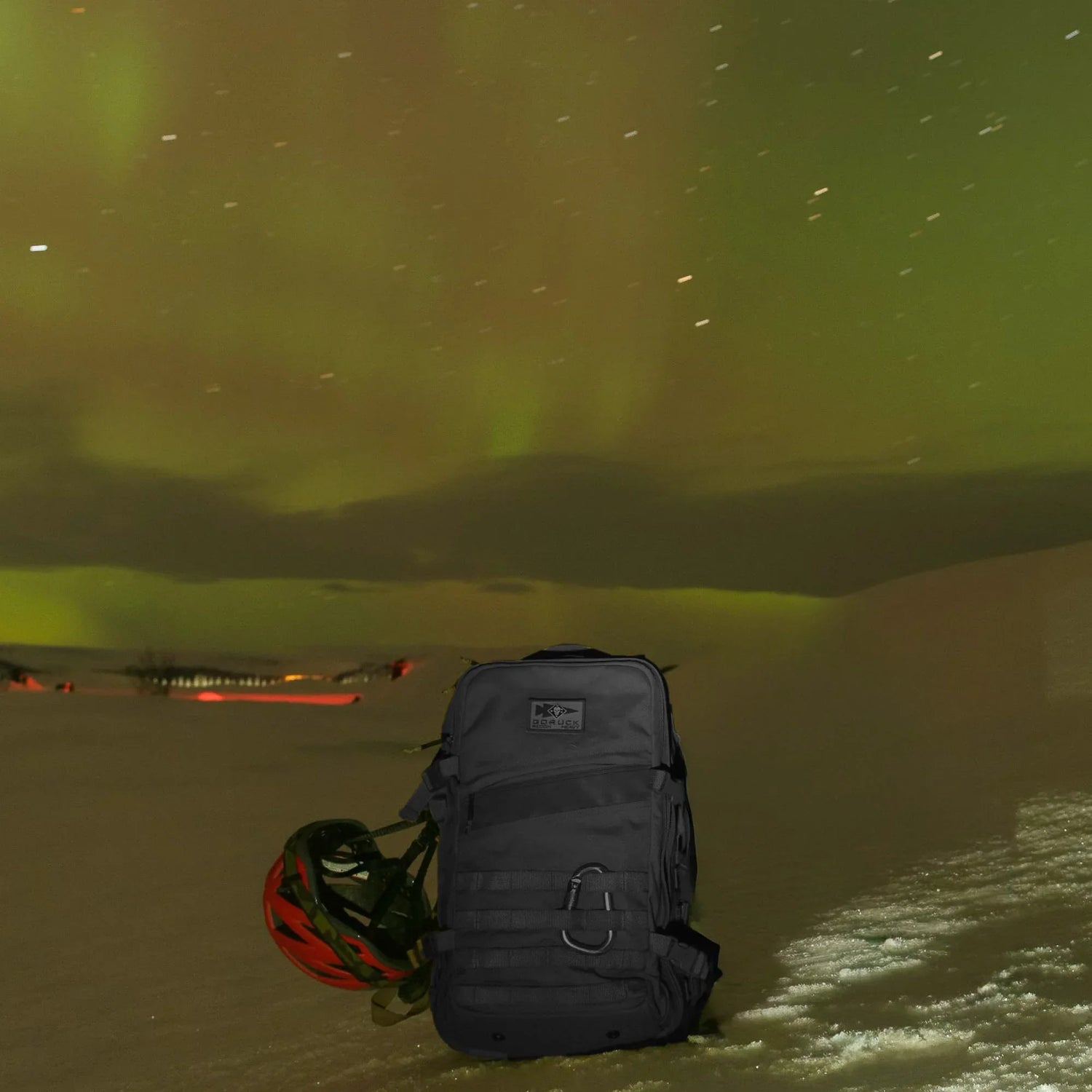 GORUCK rucksack and helmet on snow under northern lights outdoors