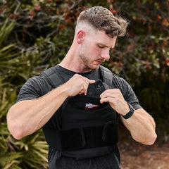 Man wearing GORUCK rucking vest outdoors, placing phone in front pocket, fitness gear