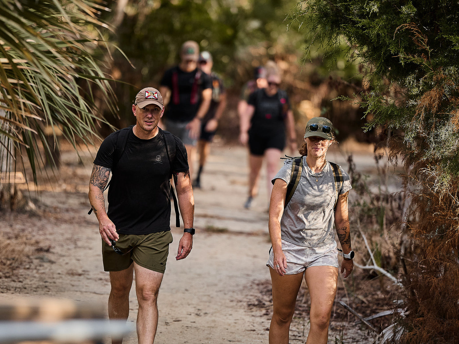 Two people hiking on a dirt trail with three others walking behind them through a wooded area.