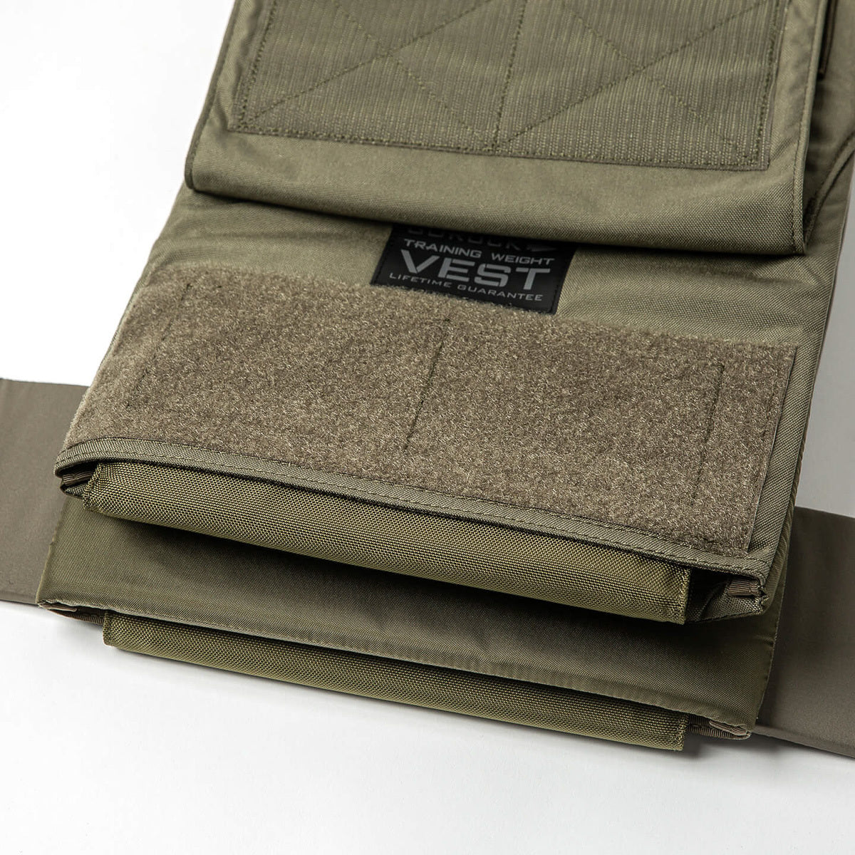 Close-up of the Training Weight Vest 2.0 in olive green, featuring Velcro straps, visible ruck plates, and a label.