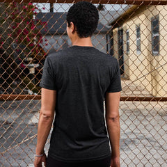 Person in dark GORUCK t-shirt standing outside by a chain-link fence, urban setting