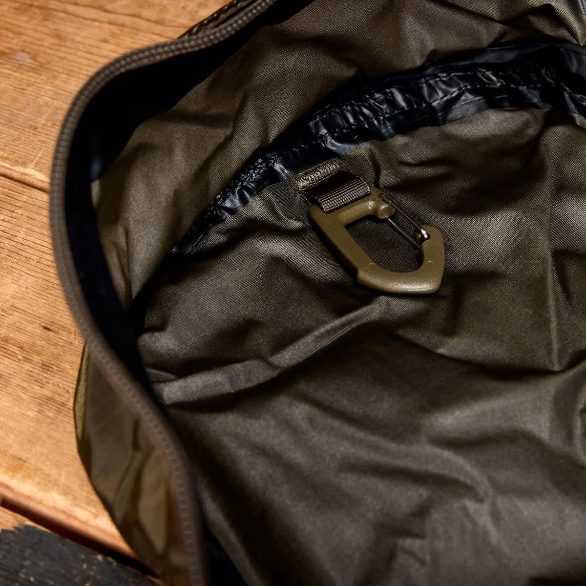 A close-up of the Packable Bullet Ruck - Ripstop ROBIC® interior with a plastic clip, displayed on a wooden surface.