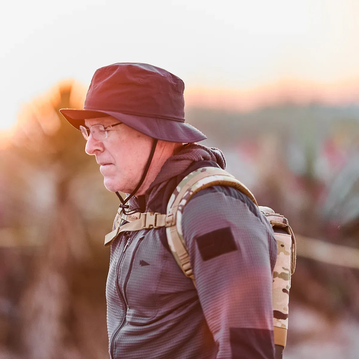Man rucking outdoors at sunrise wearing GORUCK MultiCam ruck plate carrier and bucket hat