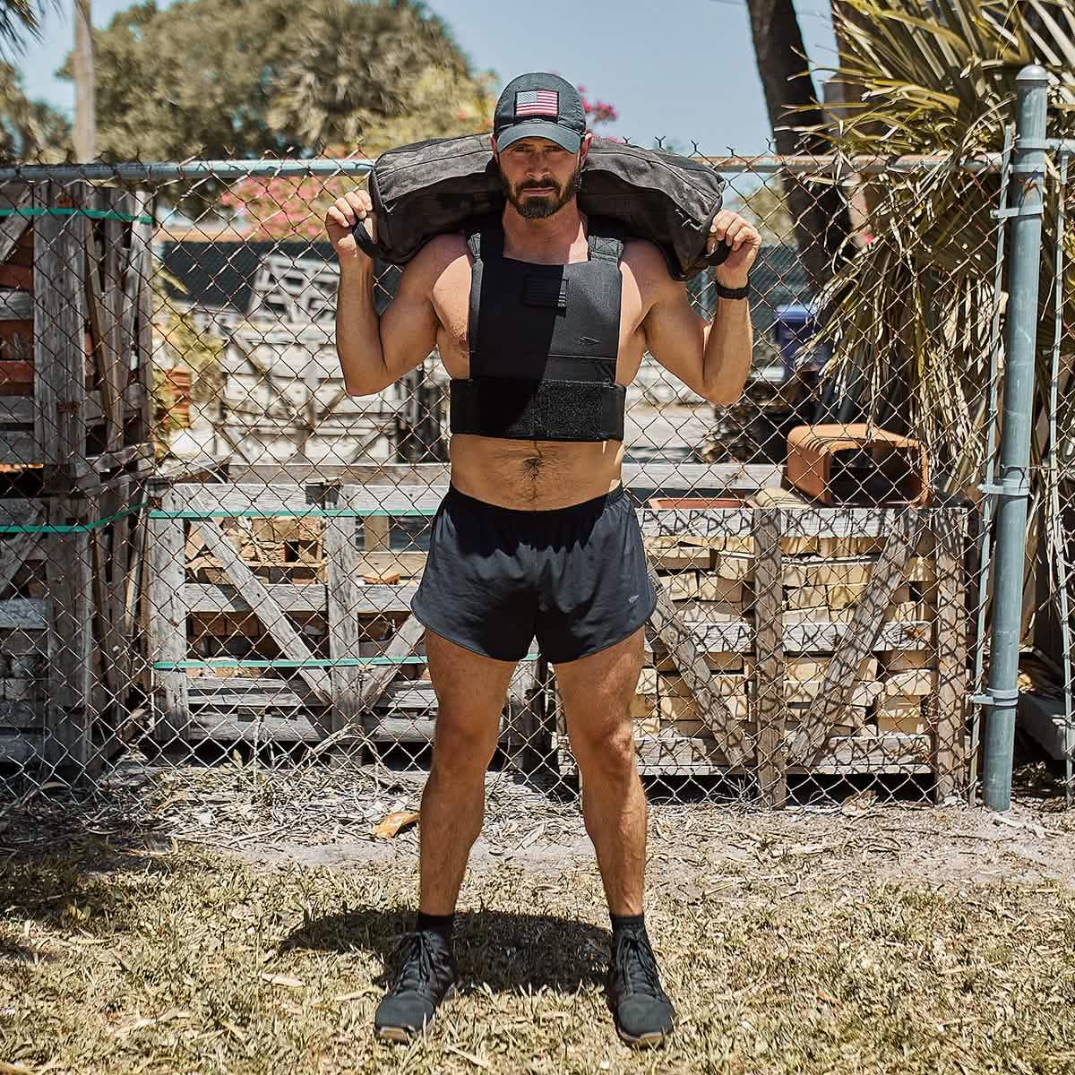 Man in GORUCK black Ranger Panties shorts, weighted vest, and cap, rucking outdoors.