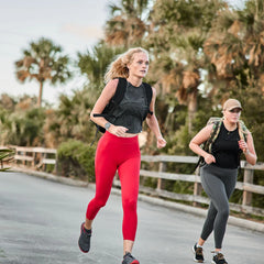 Women rucking outdoors in GORUCK gear, one wearing red leggings, palm trees in background.