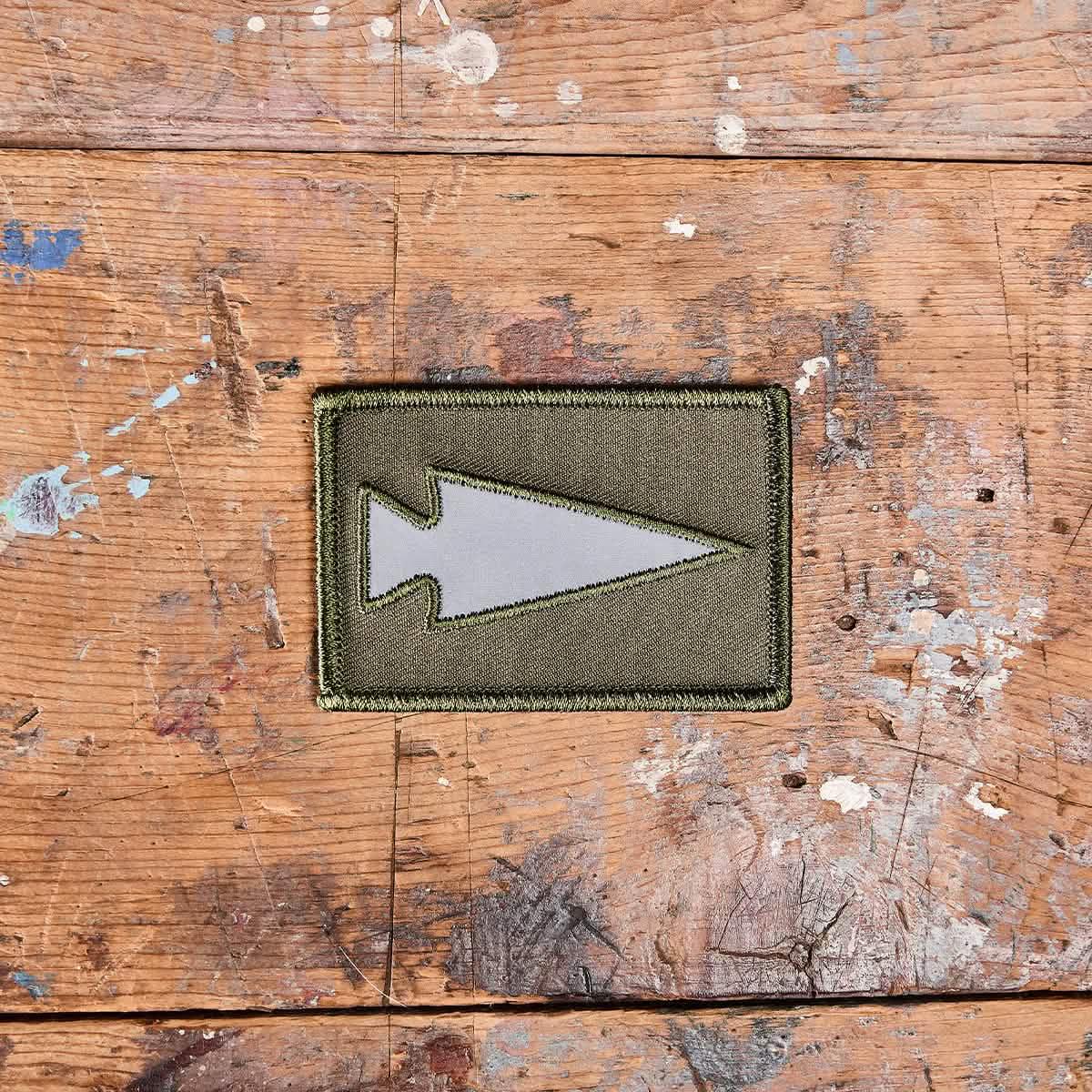 GORUCK reflective green arrowhead patch on distressed wooden surface