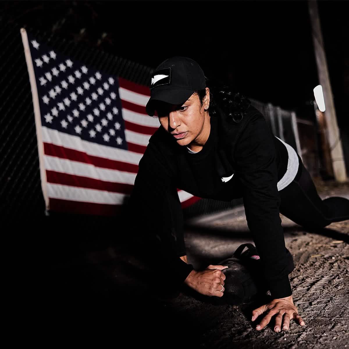 Woman in GORUCK gear training outdoors at night with an American flag backdrop