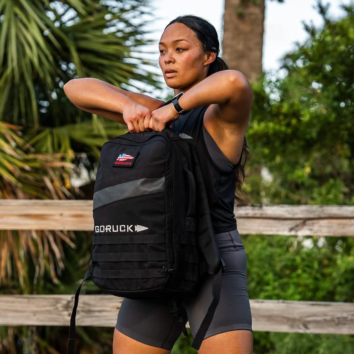 Woman outdoors wearing GORUCK ToughFlex Charcoal Bra, holding black GORUCK rucksack