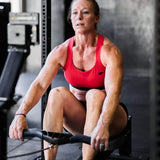 Woman working out on rowing machine in gym wearing GORUCK red sports bra